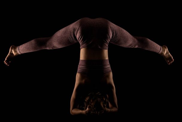 Fit woman practicing yoga poses. Side lit half silhouette girl doing exercise in studio against black background. - Foto, Imagen