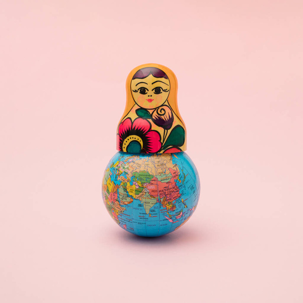 Μια σφαίρα με το πάνω μέρος μιας ρωσικής παραδοσιακής ξύλινης κούκλας. Ελάχιστη έννοια των γεγονότων στον πλανήτη. Ζυμαρικά ροζ φόντο - Φωτογραφία, εικόνα