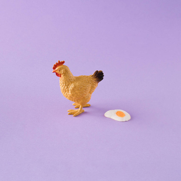 Minimal Easter concept. Brown hen and fried sunny side up egg. Purple background - Photo, Image