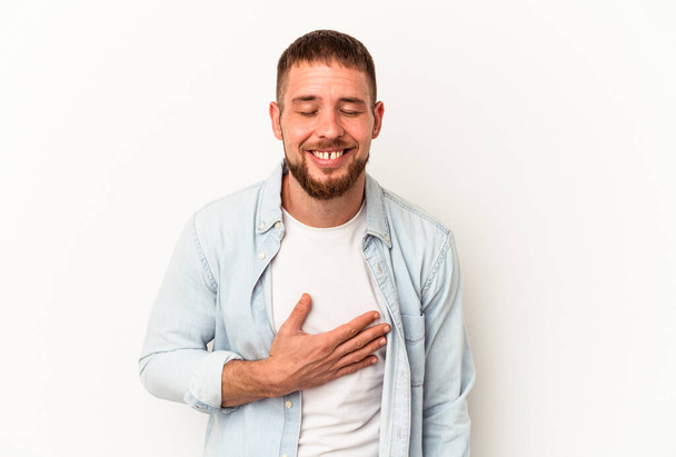 Jeune homme caucasien avec diastème isolé sur fond blanc rit bruyamment en gardant la main sur la poitrine. - Photo, image