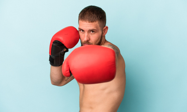 Joven hombre caucásico practicando boxeo aislado sobre fondo azul - Foto, Imagen
