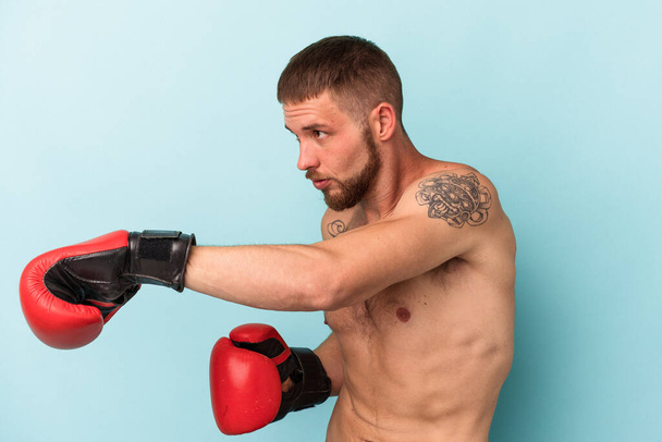青い背景に隔離されたボクシングを練習している若い白人男性 - 写真・画像