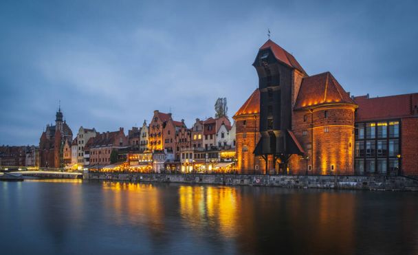 Gyönyörű építészet a régi város Gdansk a Motlawa folyó mellett egy történelmi kikötő daru éjjel. Lengyelország, 2021 november - Fotó, kép