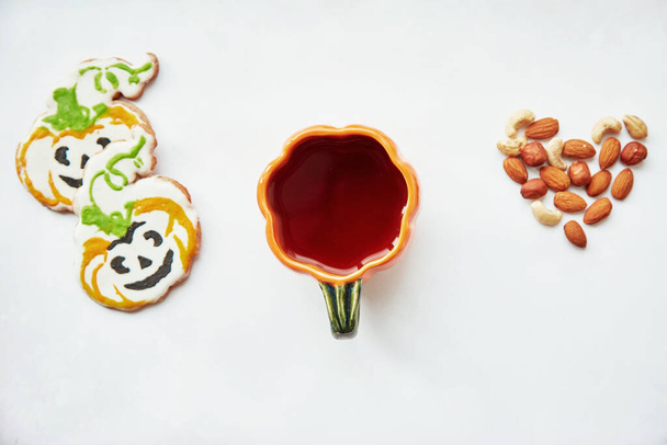 Halloween creative background: pumpkin cup and homemade cookies in shape of cute pumpkins and almonds heart. Trick or treat concept. Aesthetic autumn coziness mood. Autumn decorations. Copy space - Photo, Image
