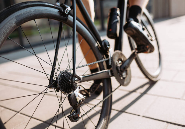 Close up de ciclista profissional com pernas musculares usando bicicleta esportiva preta para treinamento ao ar livre. Concentre-se nas rodas. Exercício regular de desportista. - Foto, Imagem