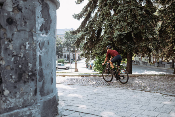 Sportlicher junger Mann in Aktivkleidung und Helm auf schwarzem Fahrrad an der frischen Luft. Kaukasischer Sportler genießt sein liebstes aktives Hobby auf der Straße. - Foto, Bild