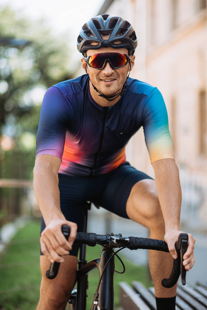 Portrait of smiling caucasian cyclist in sport clothes, helmet and glasses sitting on bike outdoors. Sunny warm day outdoors. Active workout concept. - Foto, immagini