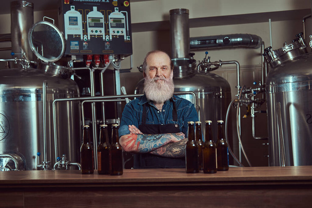 Confident old man around steel barrels indoors beer factory - Photo, Image