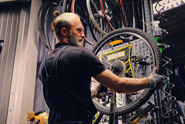 Стареющий механик фиксирует велосипедное колесо в современной мастерской - Фото, изображение