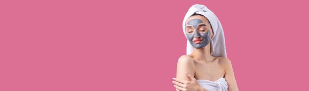 Женщина с серой глиной косметической маской в белом полотенце на голове на розовом фоне Тихого океана. - Фото, изображение