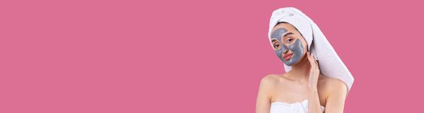 Жінка з сірою глиняною косметичною маскою в білому рушнику на голові на тихоокеанському рожевому фоні.. - Фото, зображення