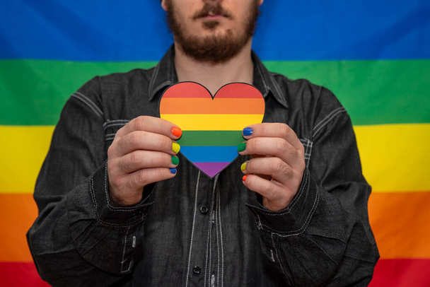 gay uomo holding un cuore con un arcobaleno bandiera su un arcobaleno fondo - Foto, immagini