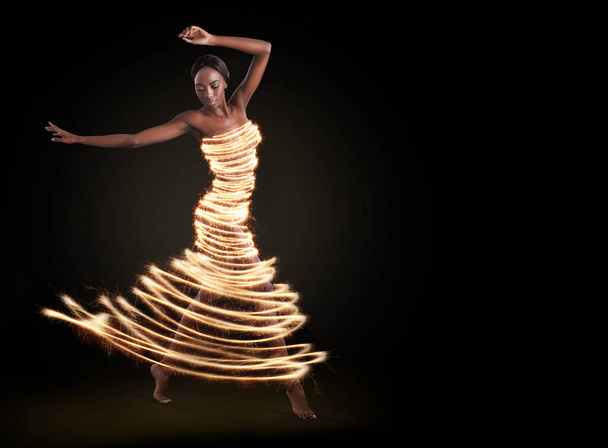 Dance to the light in your soul. Studio shot of a beautiful woman wearing a digitally enhanced dress against a black background. - Foto, Imagem