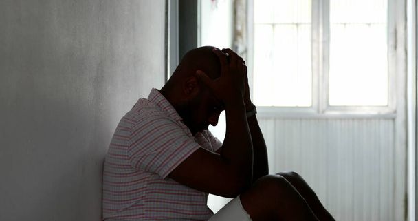 Verzweifelter schwarzafrikanischer Mann sitzt in Verzweiflung und Depression auf dem Fußboden seines Hauses - Foto, Bild
