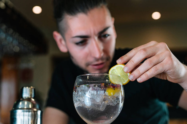 Молодой бармен украшает ломтиком цитрусовых коктейль в хрустале со льдом. - Фото, изображение