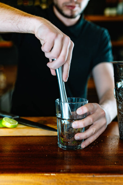 подробности рук молодого и современного официанта, раздавливающего ингредиенты мохито, чтобы выпустить соки. вертикальная - Фото, изображение