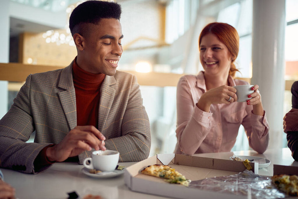 Een jonge zakenman kletst met een vrouwelijke collega terwijl ze na een lunch samen in een aangename sfeer in het bedrijfsgebouw genieten van koffie. Zaken, mensen, bedrijf - Foto, afbeelding