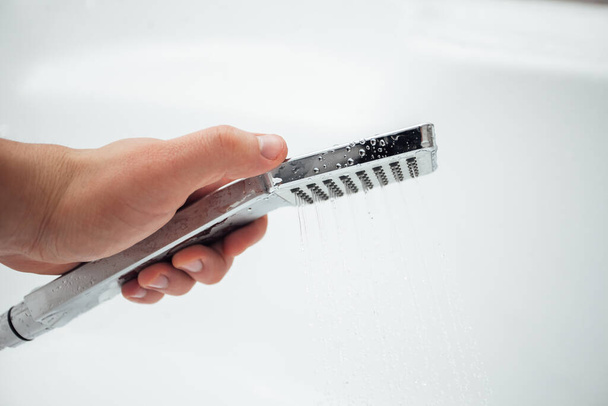 man hand houden douche tegen witte muur in badkamer, close-up schot  - Foto, afbeelding
