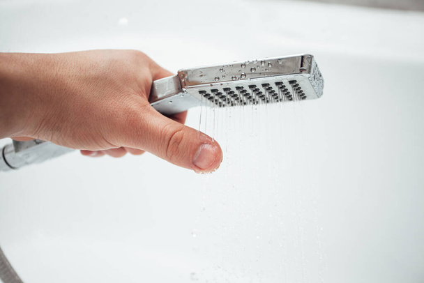 Male hand holding shower against white wall in bathroom, closeup shot  - Photo, Image