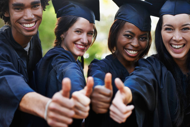 Tanulj. Egy csapat mosolygó főiskolai diplomás adja fel a hüvelykujját a diplomaosztón.. - Fotó, kép