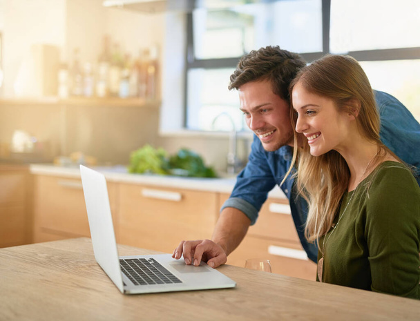 Encontrar una receta que ambos puedan disfrutar. Fotografía de una joven pareja sonriente usando un ordenador portátil en el mostrador de su cocina en casa. - Foto, Imagen