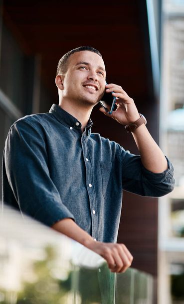 Es hora de que publiques tu nombre. Fotografía de un joven hombre de negocios parado en el balcón de una oficina y usando un teléfono inteligente. - Foto, imagen
