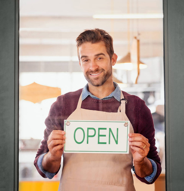 Entrez donc. Portrait d'un jeune propriétaire d'entreprise debout à la porte de son café avec un panneau ouvert. - Photo, image
