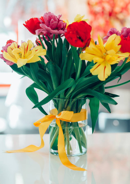 Knotted bow on a vase, flowers in water, tulips in different colors, home decoration - Photo, Image