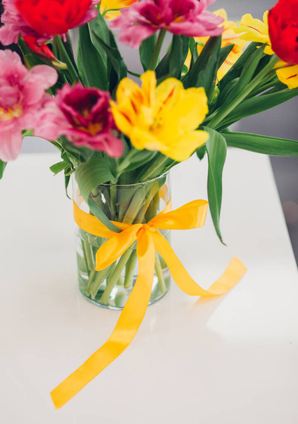 Knotted bow on a vase, flowers in water, tulips in different colors, home decoration - Photo, Image