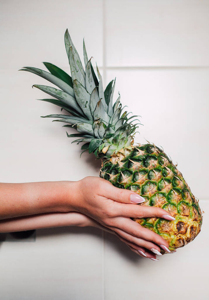 Female hands holding ripe pineapple on a white background - Фото, изображение