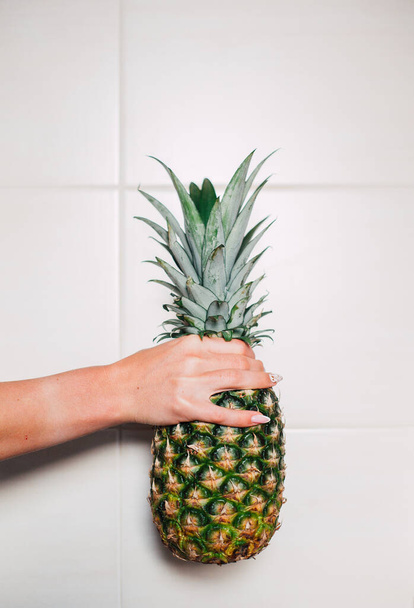 Female hands holding ripe pineapple on a white background - 写真・画像