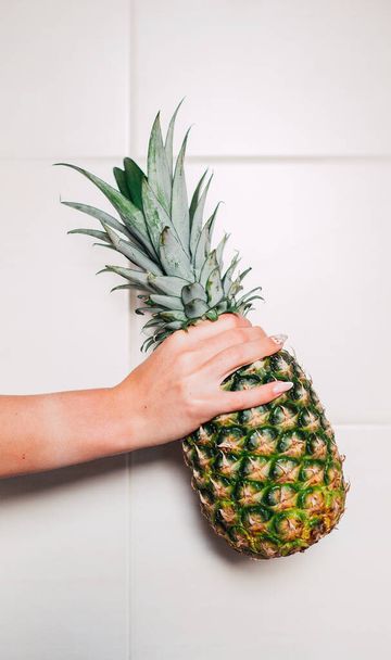 Female hands holding ripe pineapple on a white background - Foto, Imagen