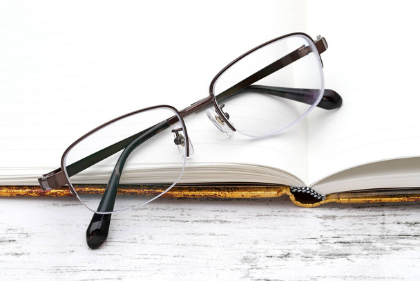 Óculos de visão elegantes e caderno aberto na mesa de madeira branca  - Foto, Imagem