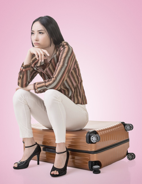 Mulher asiática pensando e sentado em uma bagagem
 - Foto, Imagem