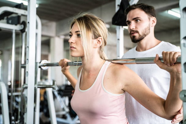 Smart sport women lift up barbell with trainer man in gym healthy concept - Foto, imagen