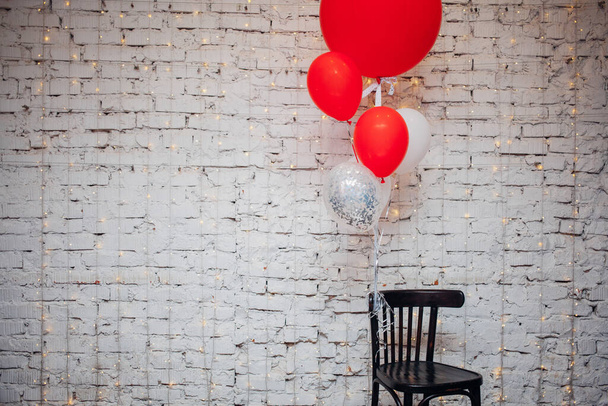 Holzsessel und große bunte Luftballons auf weißem Backstein-Hintergrund  - Foto, Bild