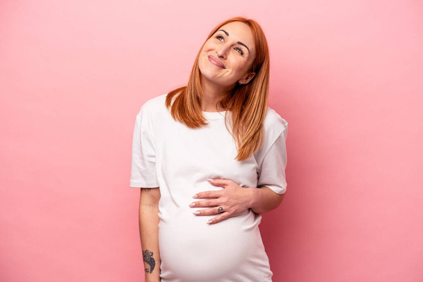 Νεαρή καυκάσια έγκυος γυναίκα απομονωμένη σε ροζ φόντο ονειρεύεται την επίτευξη στόχων και σκοπών - Φωτογραφία, εικόνα