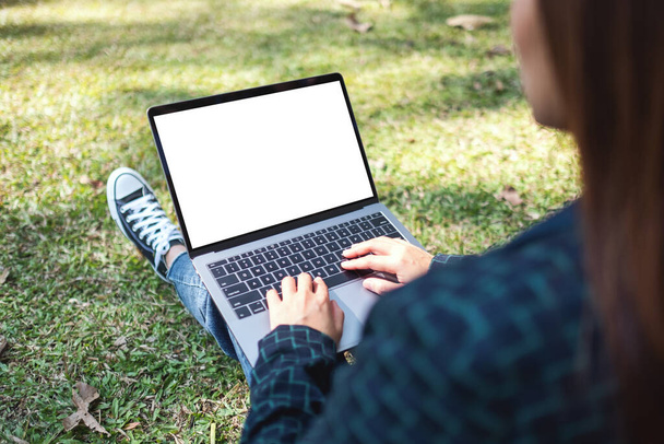 Makieta kobiety używającej i piszącej na laptopie z białym ekranem, siedzącej na świeżym powietrzu z tłem natury - Zdjęcie, obraz