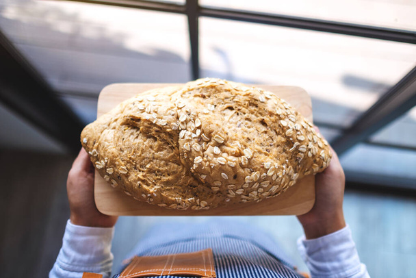 Top view image of a waitress holding and serving a loaf of whole grain bread - Photo, Image