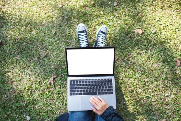 Top view mockup image of a woman using and typing on laptop with blank white screen while sitting in the outdoors  - Foto, Bild