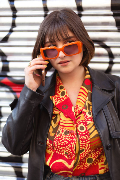 Beautiful young caucasian woman talking on phone outdoors. She wears a cute trendy outfit and sunglasses. Modern urban fashion concept. - Фото, зображення