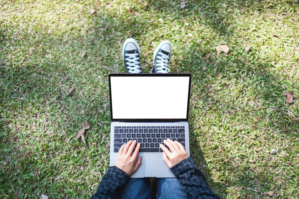 Mockup-Bild einer Frau, die im Freien sitzt und auf Laptop mit leerem weißen Bildschirm tippt - Foto, Bild