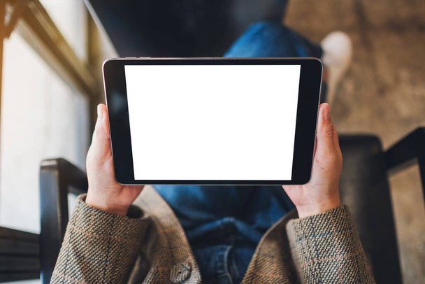 Visualizzazione dall'alto immagine mockup di una donna seduta e con in mano tablet pc nero con schermo desktop bianco vuoto
  - Foto, immagini