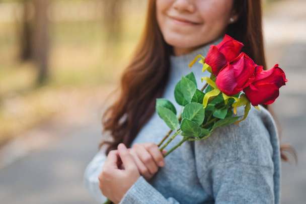 Closeup image of a beautiful asian woman holding red roses flower with feeling happy on Valentine's day - Photo, Image