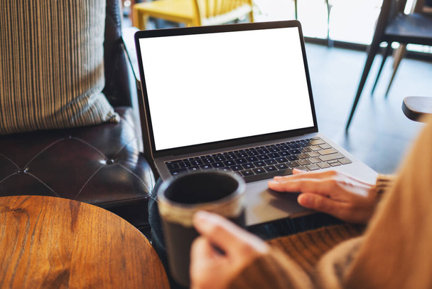 Mockup-Bild einer Frau, die beim Kaffeetrinken ein Laptop-Touchpad mit leerem weißen Desktop-Bildschirm benutzt und berührt - Foto, Bild