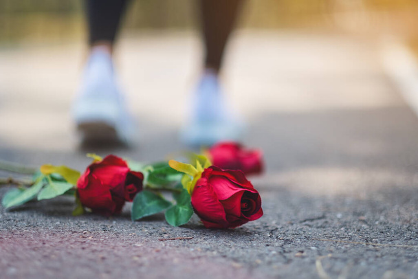 Eine Frau dreht sich um und geht weg von roten Rosen, die auf dem Boden blühen - Foto, Bild