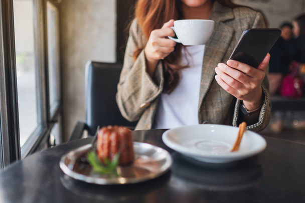 Zbliżenie obrazu azjatki trzymającej i używającej telefonu komórkowego podczas picia kawy w kawiarni - Zdjęcie, obraz