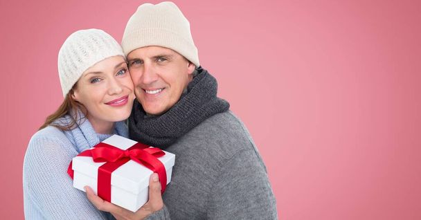 Portrait of caucasian couple holding a gift box and smiling against copy space on pink background. christmas festivity and celebration concept - Foto, immagini
