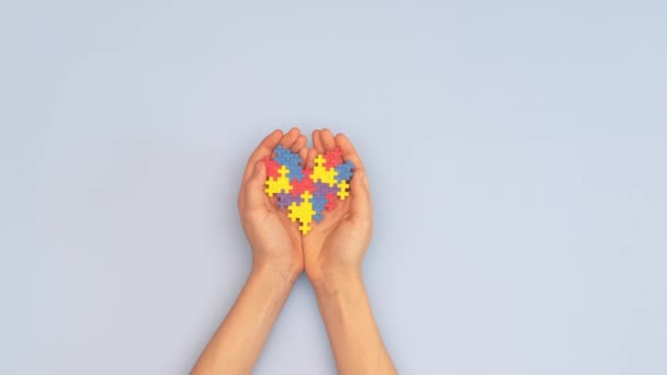 Концепция Всемирного дня аутизма. Женщина и ребенок держат в руках сердце-головоломку на голубом фоне. Вид сверху - Кадры, видео