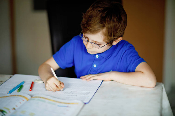 Portré a szemüveges kisfiúról, aki házi feladatot csinál, színes tollakkal ír leveleket. Egy kisgyerek gyakorol a házban. Általános iskola és oktatás, otthoni oktatás koncepciója. - Fotó, kép